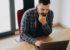 pexels-photo-2102415-2102415 Young man with beard working on laptop at desk in a modern office setting.